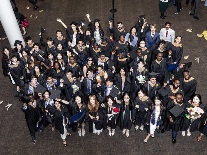 A large group of graduates in caps and gowns pose for an overhead camera at Goizueta Commencement 2024